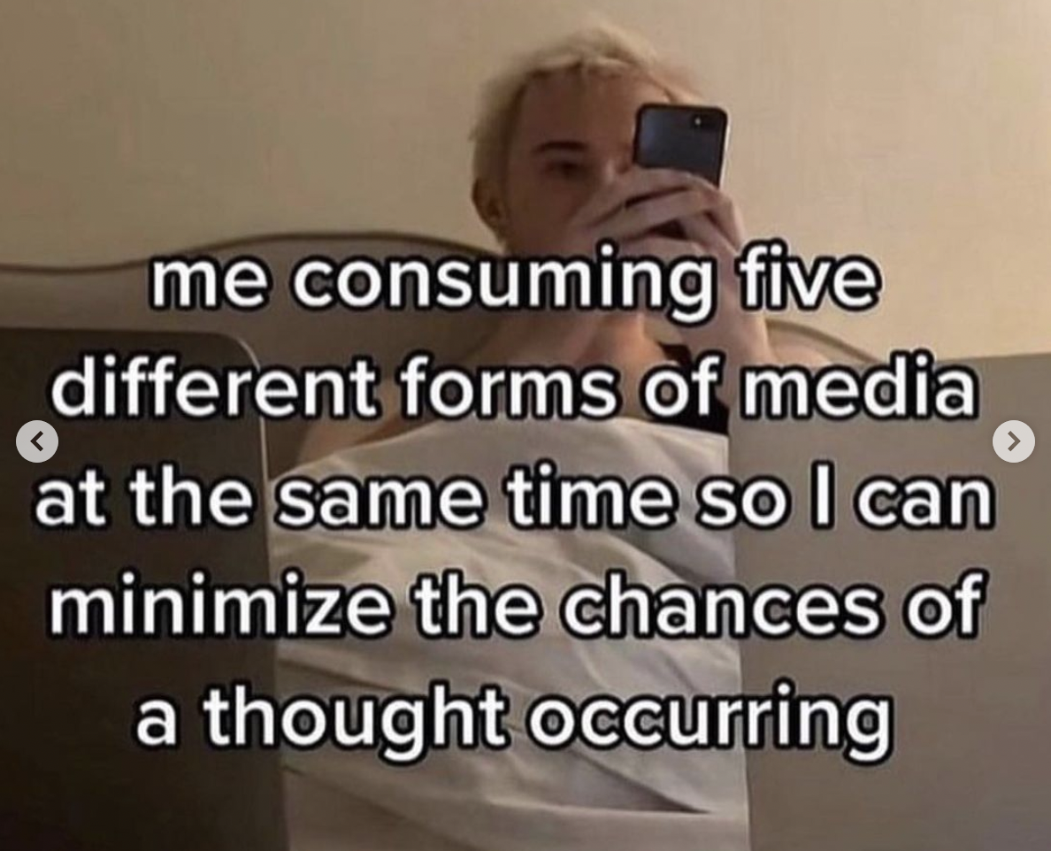 Someone in bed on their phone with this text on the image: “me consuming five different forms of media at the same time so I can minimise the chances of a thought occurring”