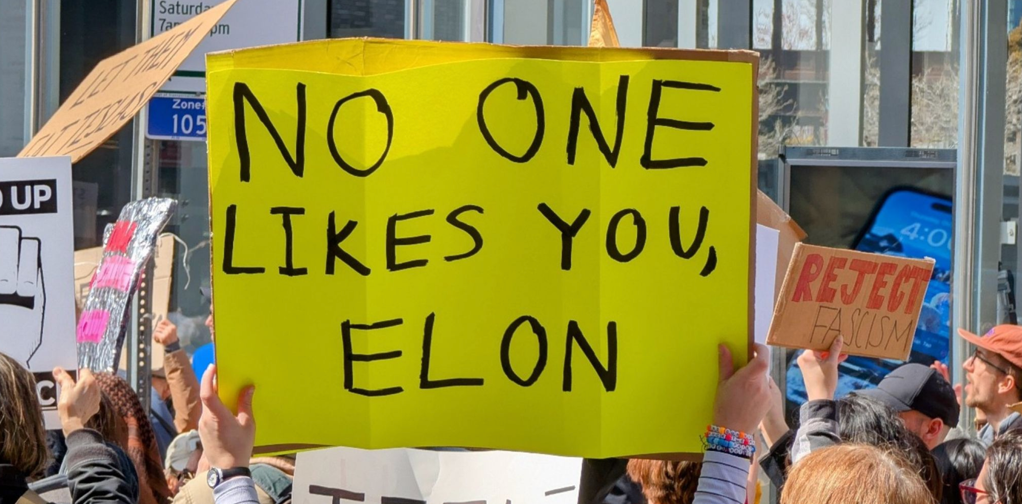 Someone holds up a "No One Likes You Elon" sign