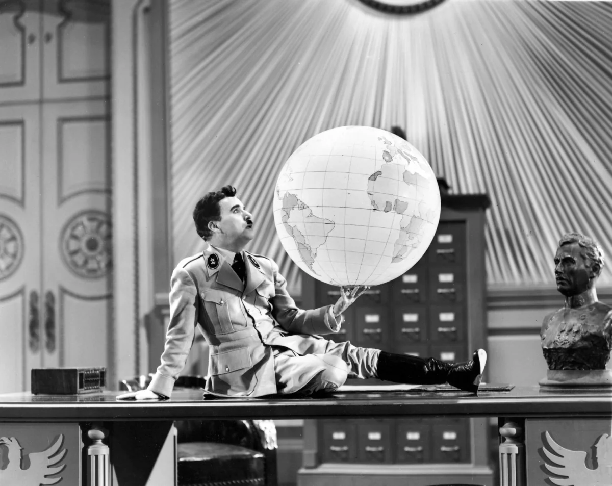 A film still from Chaplin's The Great Dictator. Adenoid Hynkel sits on his gleaming desktop and stares longingly at an illuminated globe of the world in his hands.