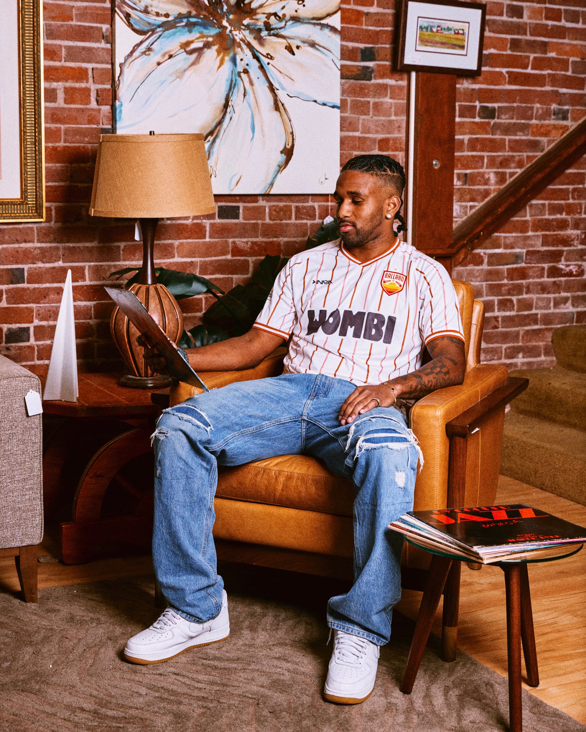 A young man sits in a padded arm chair wearing a pinstriped Ballard FC Kit