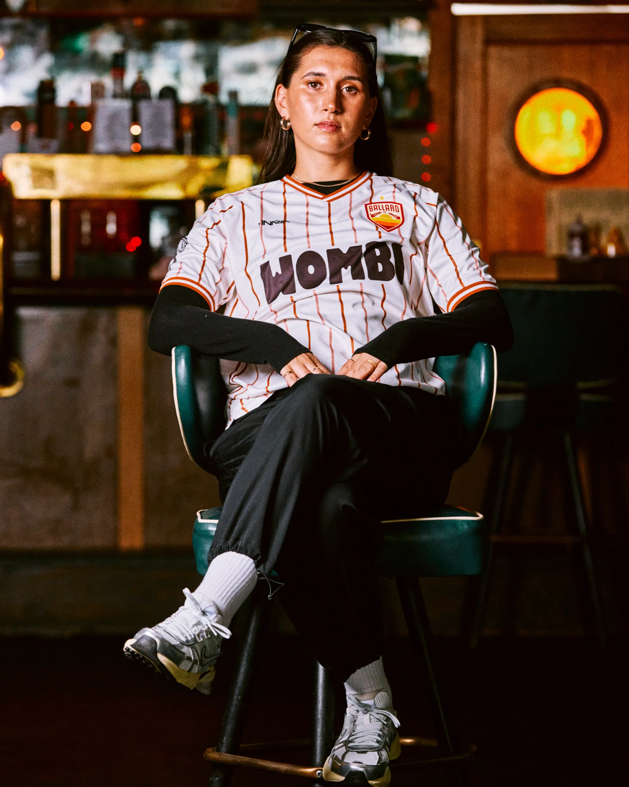 Olivia Van Der Jagt sits in a teal chair wearing a pinstriped Ballard FC jersey