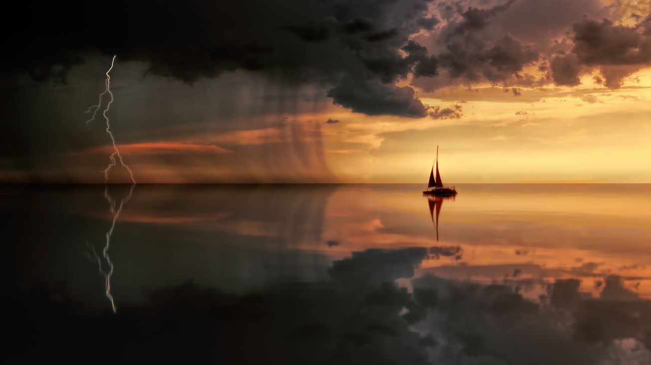 A loan sail boat at sunset on calm waters sails towards a storm with lightning in the distance.