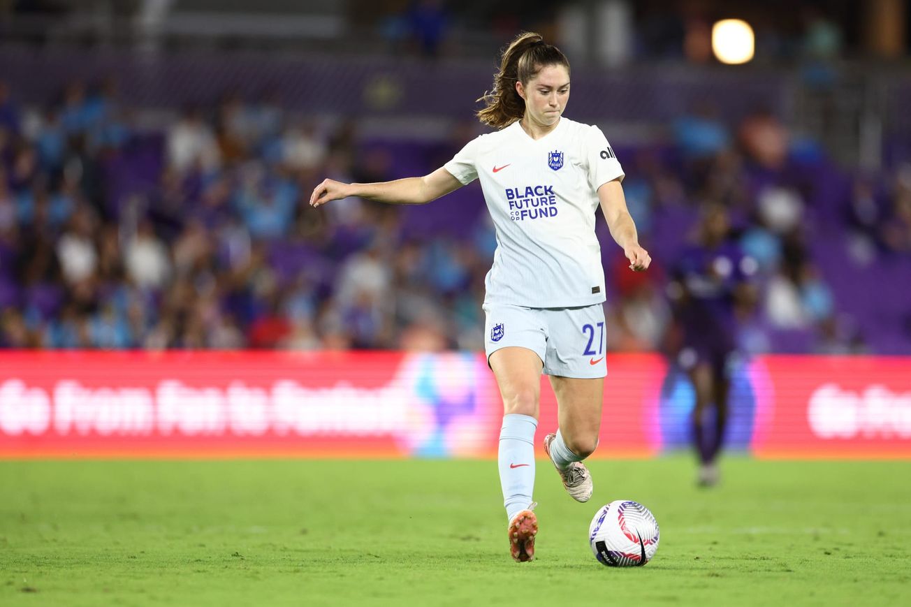 Maddie Mercado, wearing the white Seattle Reign kit, is midstride and about to strike the ball with her right foot.