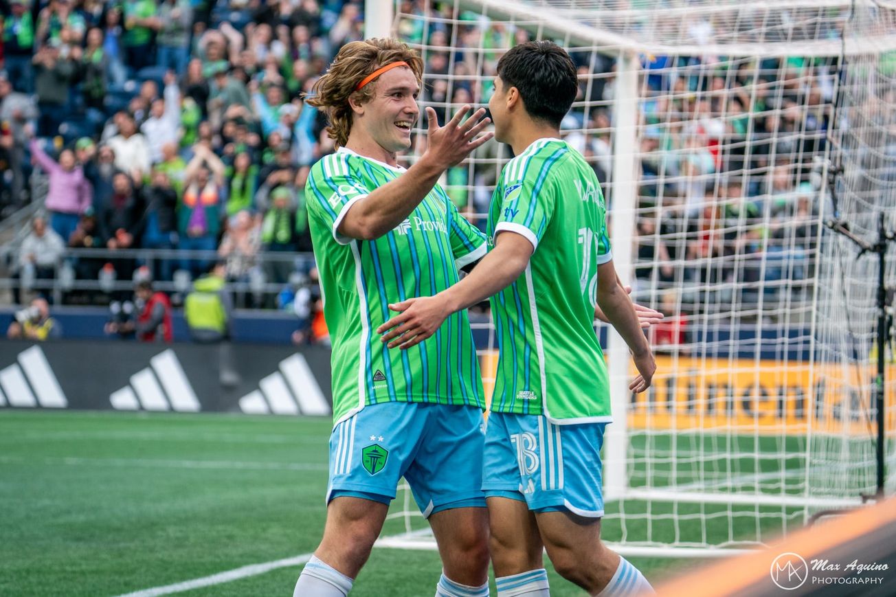 Pedro de la Vega and Obed Vargas wearing green Sounders jerseys and blue shorts, celebrating a goal