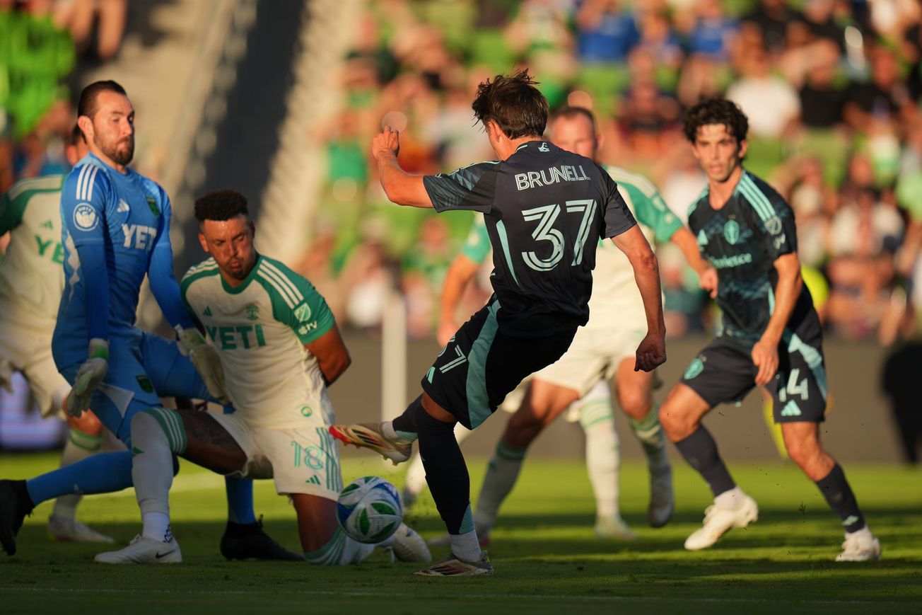 Snyder Brunell, in a dark blue Sounders kit, shoots a ball at the Austin FC goalkeeper