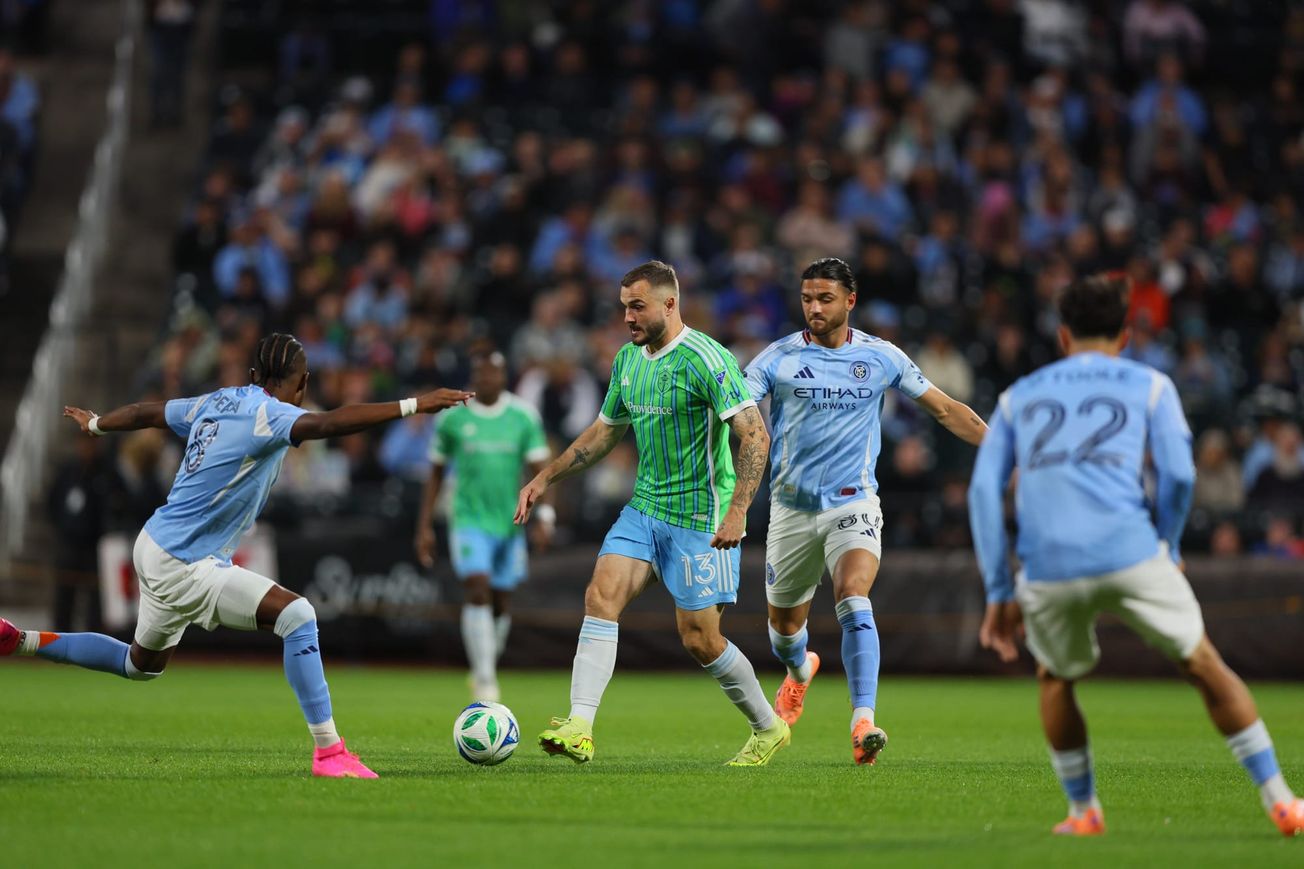Jordan Morris in a green Sounders jersey and blue shorts dribbles surrounded by defenders