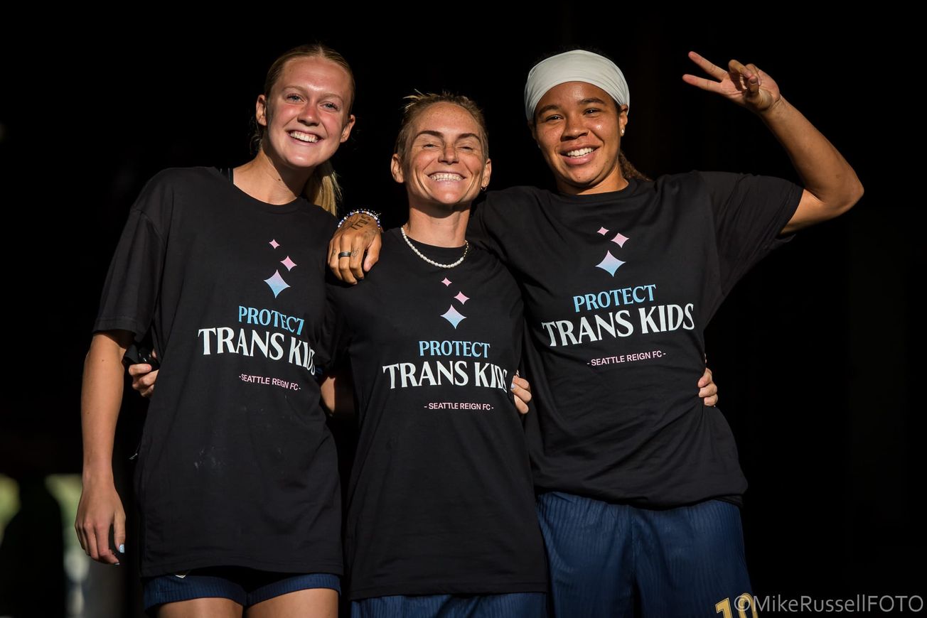 Maddie Dahlien, Jess Fishlock and Mia Fishel pose for the camera while wearing ‘Protect Trans Kids’ shirts ahead of a Seattle Reign vs. Angel City FC game in August 2025.