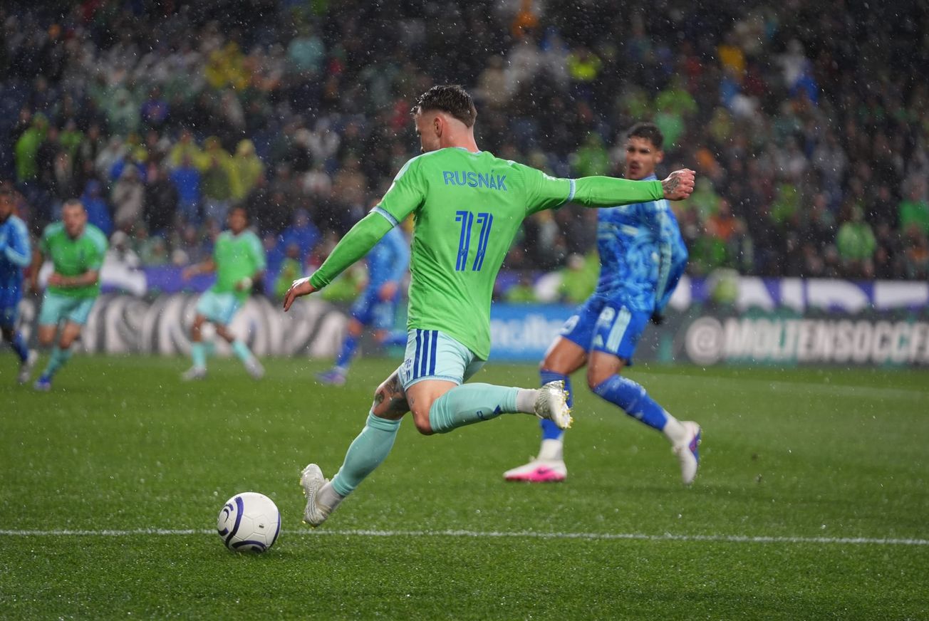 Albert Rusnák in a green Sounders jersey and light blue shorts and socks prepares to kick a ball.