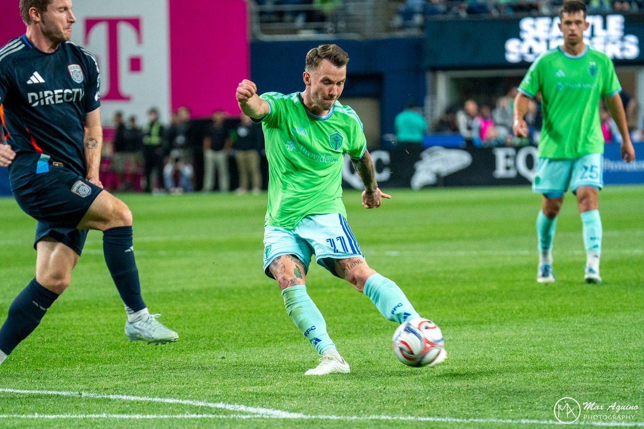 Albert Rusnak wearing a green Sounders jersey and light blue shorts and socks kicks a ball with his left foot.