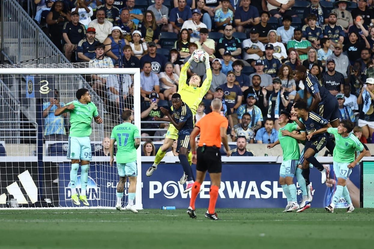 Andrew Thomas in a yellow kit jumps to grab the ball while a Philadelphia player in navy blue collides with him