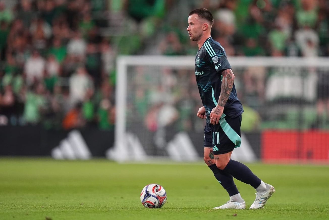 Albert Rusnák wearing a dark blue Sounders jersey with a ball in front of him.
