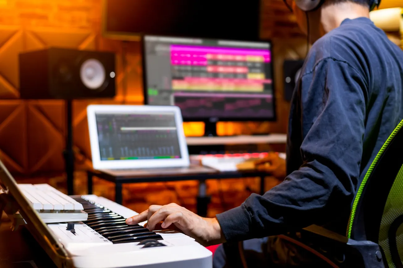Music producer playing MIDI keyboard with digital audio workstation on screen – Modern music composition and sound design in recording studio.