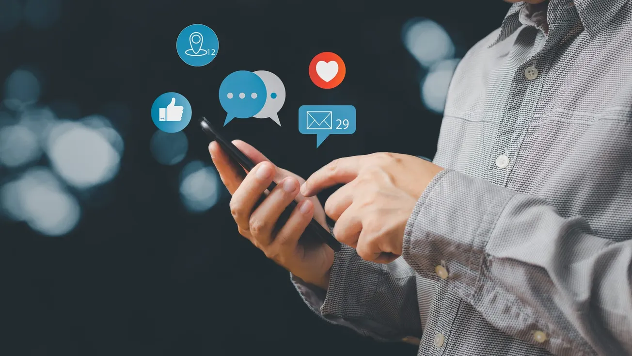 Person using smartphone with social media notification icons – Messaging, likes, and online engagement concept.