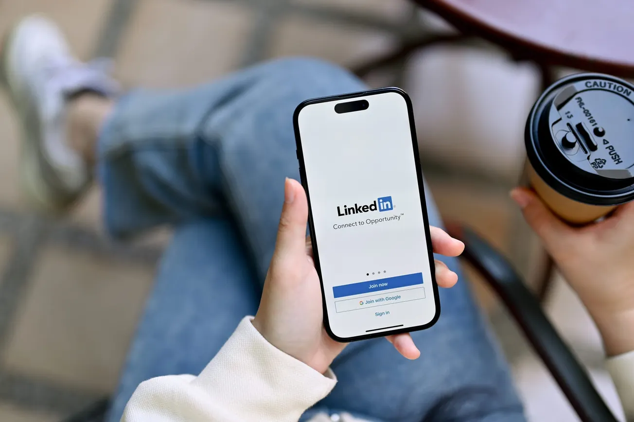 A woman's hands holding a smartphone with LinkedIn logo, sign in or register on LinkedIn