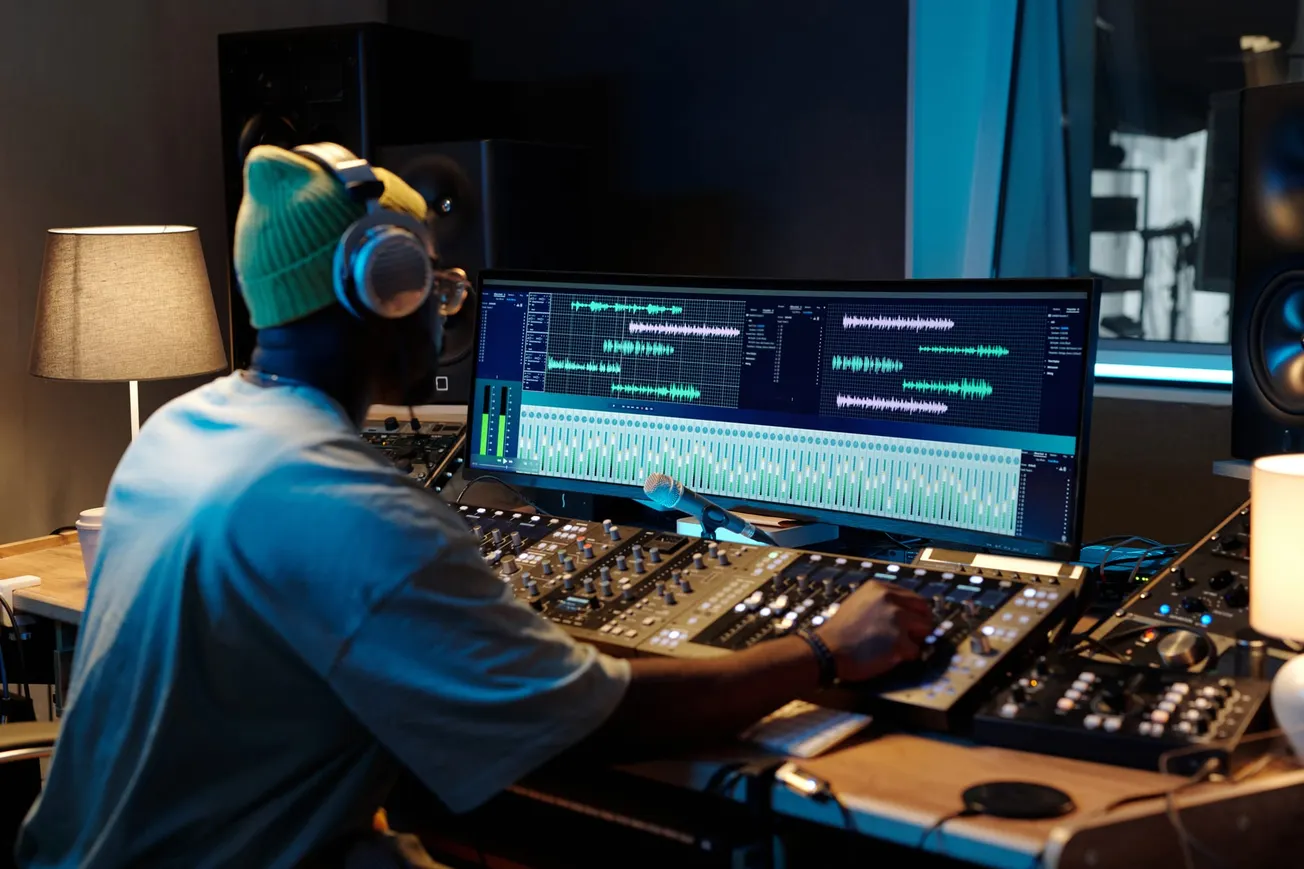 Audio engineer working at mixing console with digital audio workstation on screen – Music production and sound editing in professional studio.