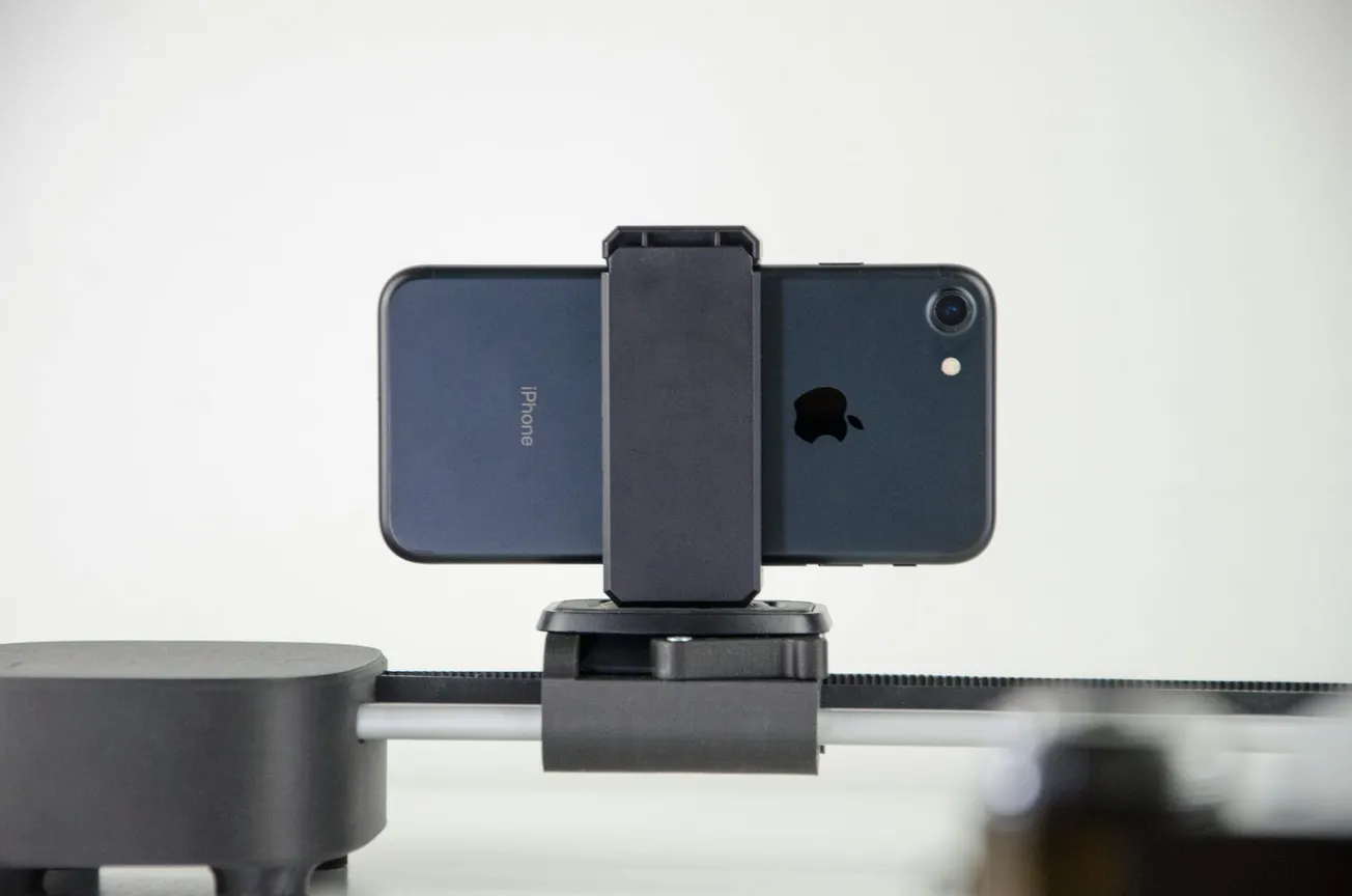 Smartphone on a motorized slider. A black phone is secured on a horizontal track, suggesting movement for smooth video capturing.