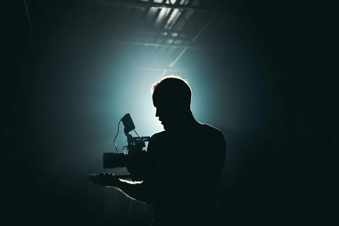 Silhouette of a person holding a camera against a dimly lit background with soft lighting.