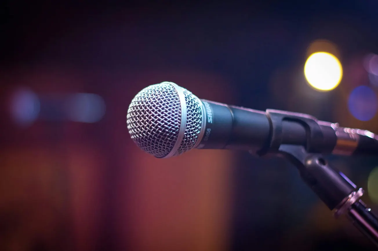 A close-up of a microphone on a stand against a blurred background with colorful lights.