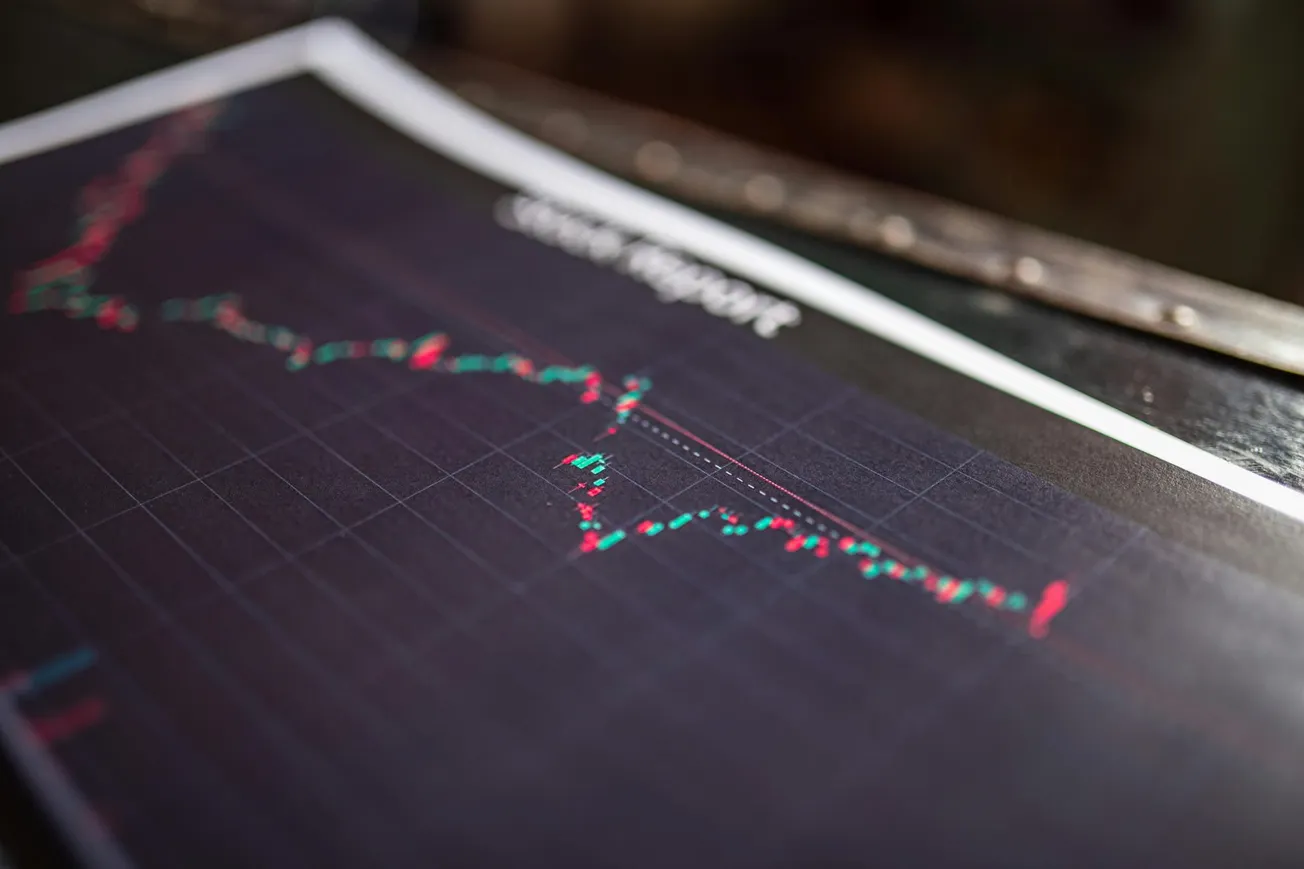 Close-up of a printed financial chart with red and green candlestick patterns on a dark background, suggesting stock market activity and analysis.