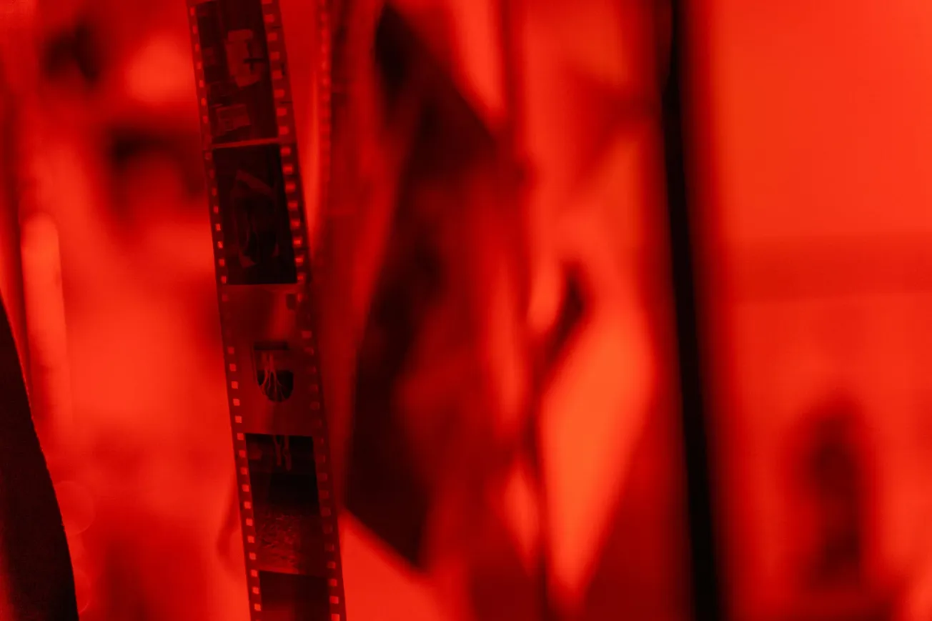 Close-up of film negatives hanging in a dimly lit darkroom, bathed in a red glow. 