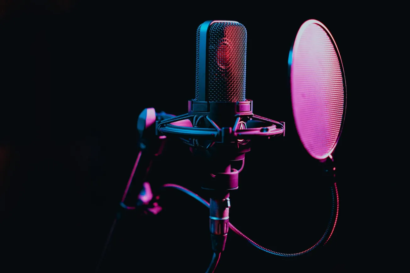 A studio microphone and pop filter are bathed in moody purple and pink lighting against a dark background, conveying a creative and professional atmosphere.
