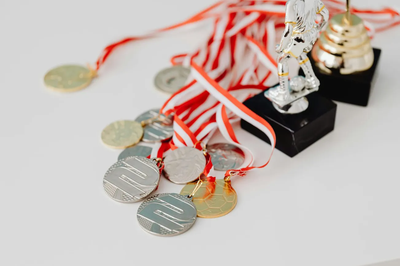 Medals with red and white ribbons are spread on a table near two trophies, suggesting triumph and celebration.