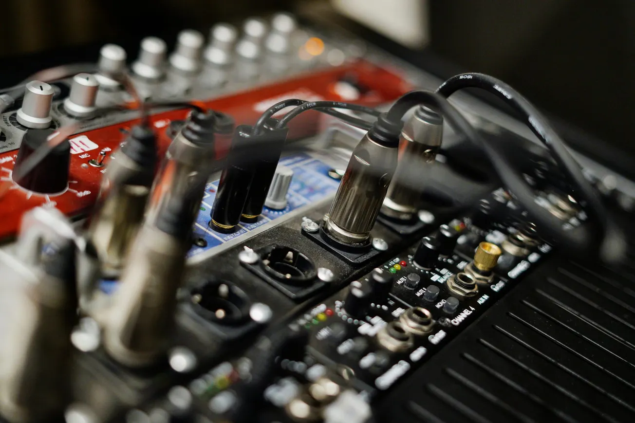 Close-up of audio equipment featuring a red soundboard with numerous knobs and cables plugged in.