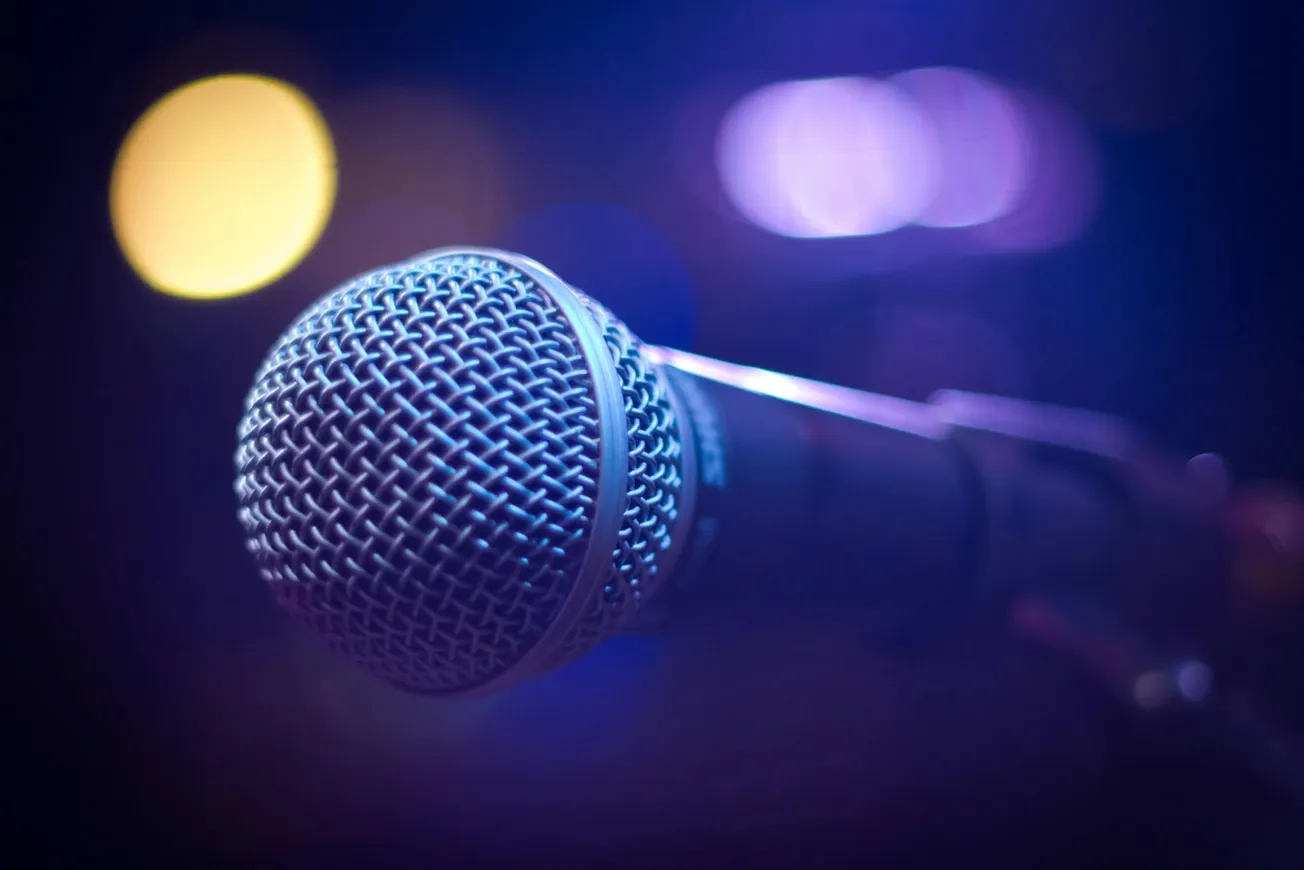 Close-up of a microphone under blue and purple stage lights, creating a moody, performance-ready atmosphere with a soft bokeh background.