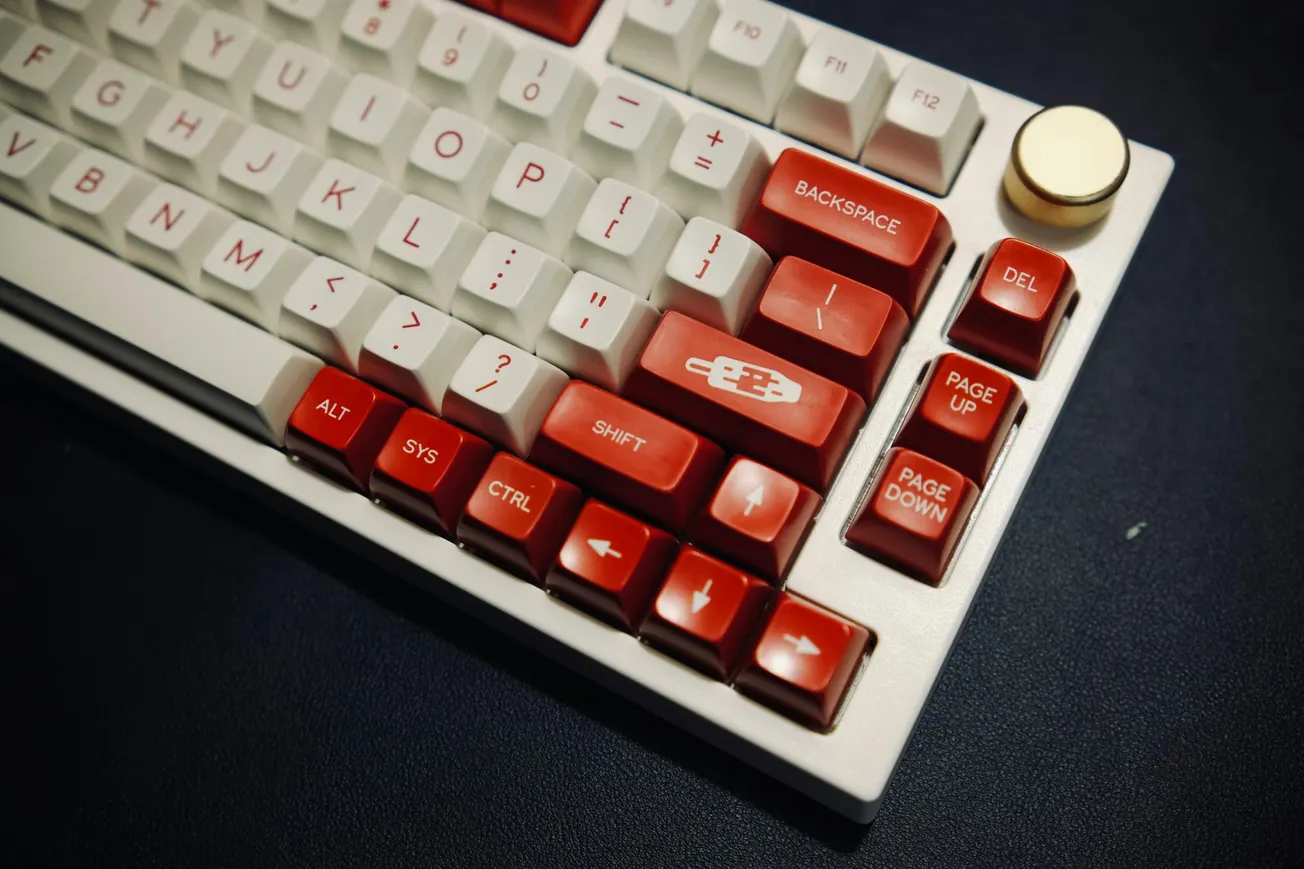 A customizable mechanical keyboard with red and white keycaps on a dark surface. Gold volume knob on top right.
