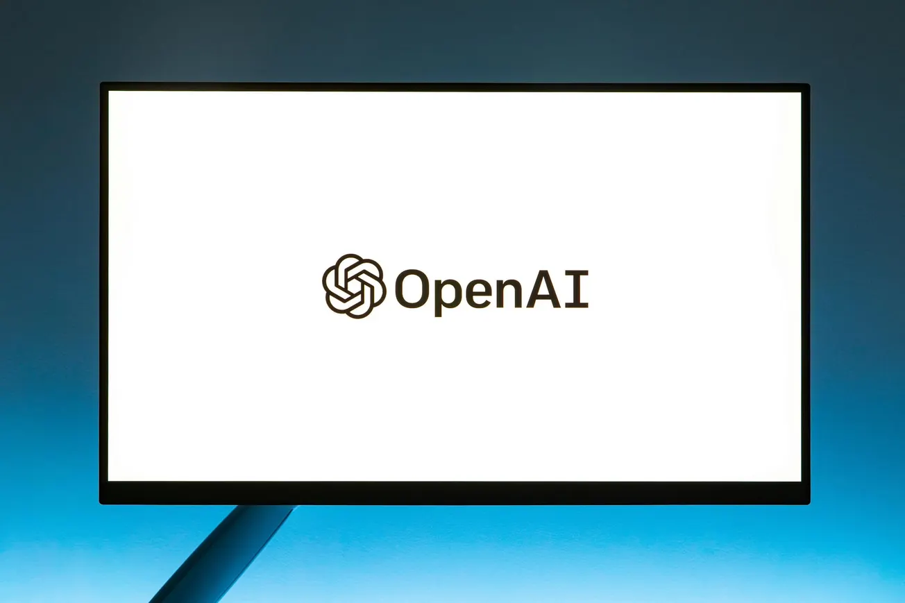 A bright screen displays the OpenAI logo on a white background, centered amidst a dark gradient backdrop. The atmosphere is modern and tech-focused.
