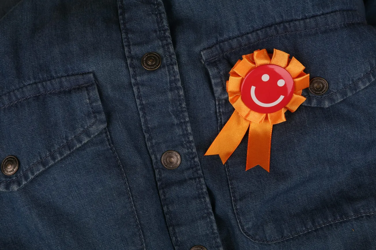Denim shirt with orange smiley face ribbon pinned to the pocket, conveying a cheerful and positive mood.