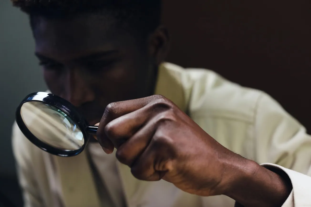 A person in a light shirt intently examines something through a magnifying glass, creating a focused and investigative atmosphere.