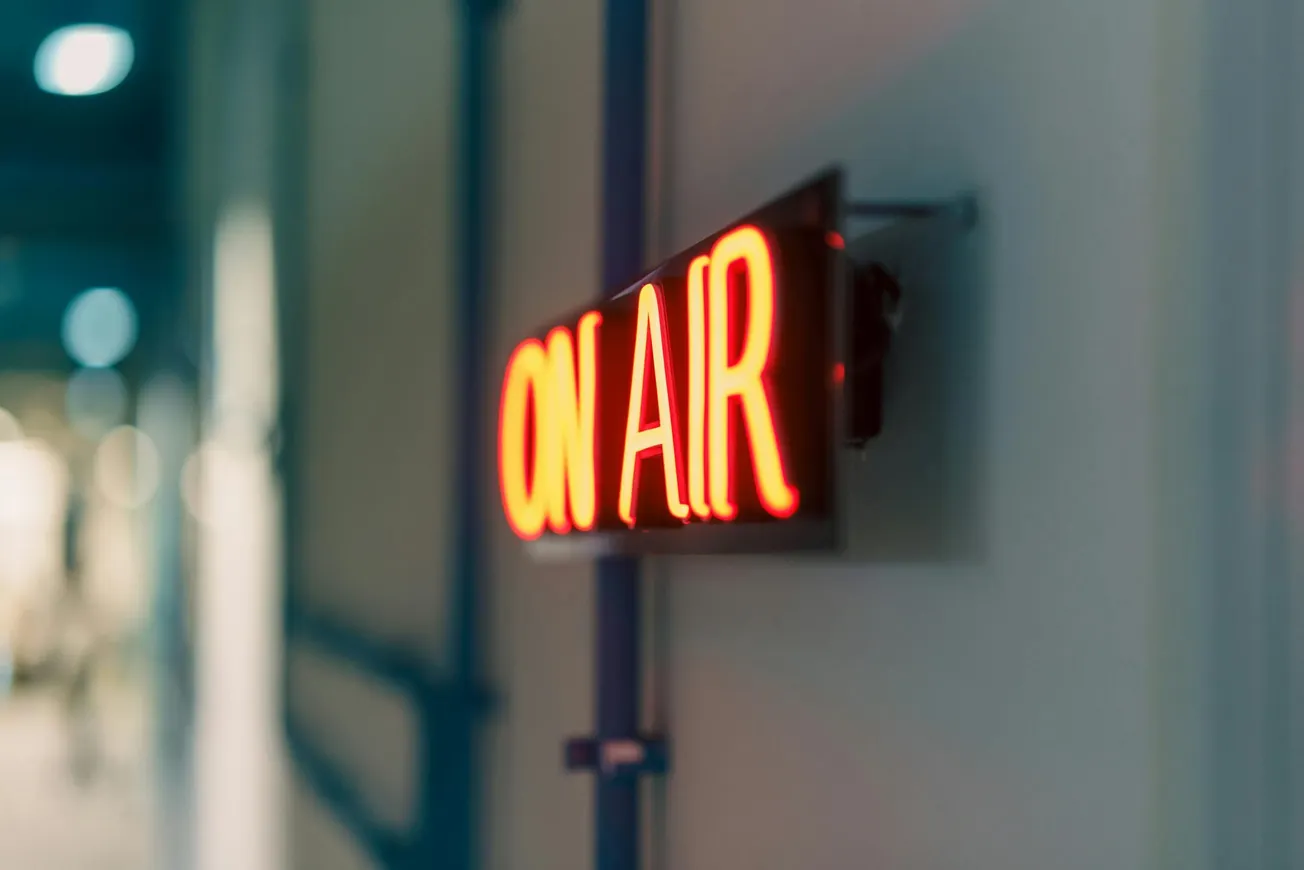 A glowing red "ON AIR" sign is mounted on a wall in a hallway, conveying a professional and active broadcasting environment.