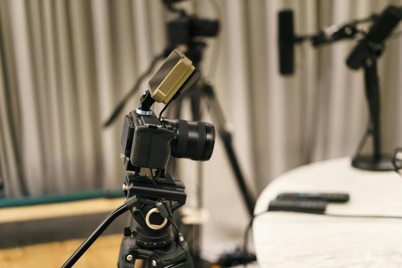 Camera on tripod with microphone, set up in a recording studio. Background includes more microphones and curtains, creating a professional ambiance.