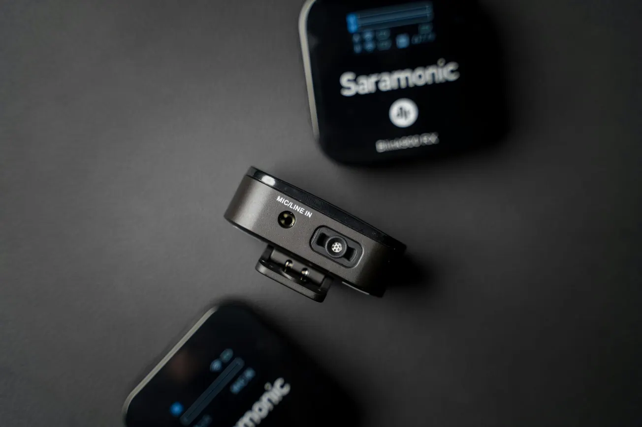 Close-up of three black Saramonic devices on a dark surface. A central device shows input ports with "Mic/Line In" text.