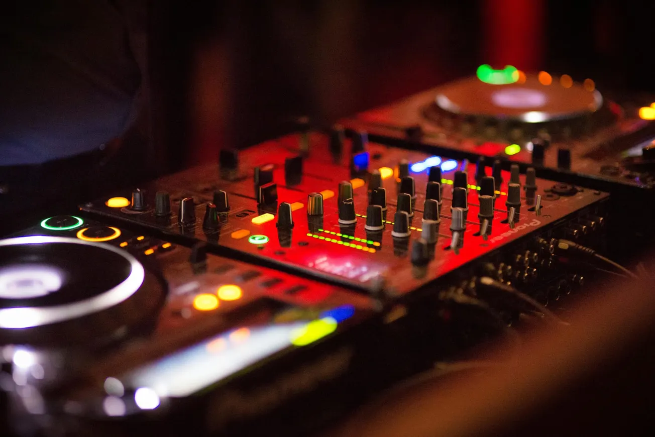 Close-up of a DJ mixing console with brightly lit controls and dials, glowing in red and green.
