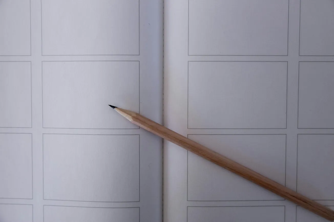 A sharpened pencil rests on an open notebook with blank rectangular frames, suggesting a storyboard or comic layout.