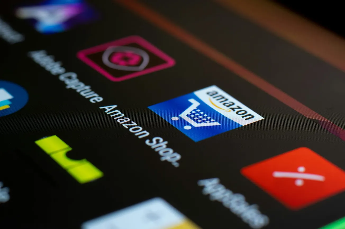 Close-up of a smartphone screen displaying various app icons, including the Amazon Shopping app with a blue cart logo, giving a modern, tech-focused feel.