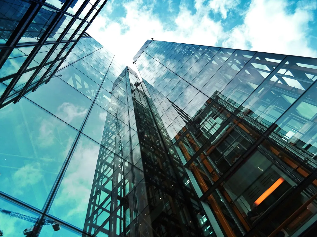 Dramatic view of modern glass skyscrapers reflecting clouds, shot from below. The upward angle emphasizes height, conveying a sense of awe and ambition.