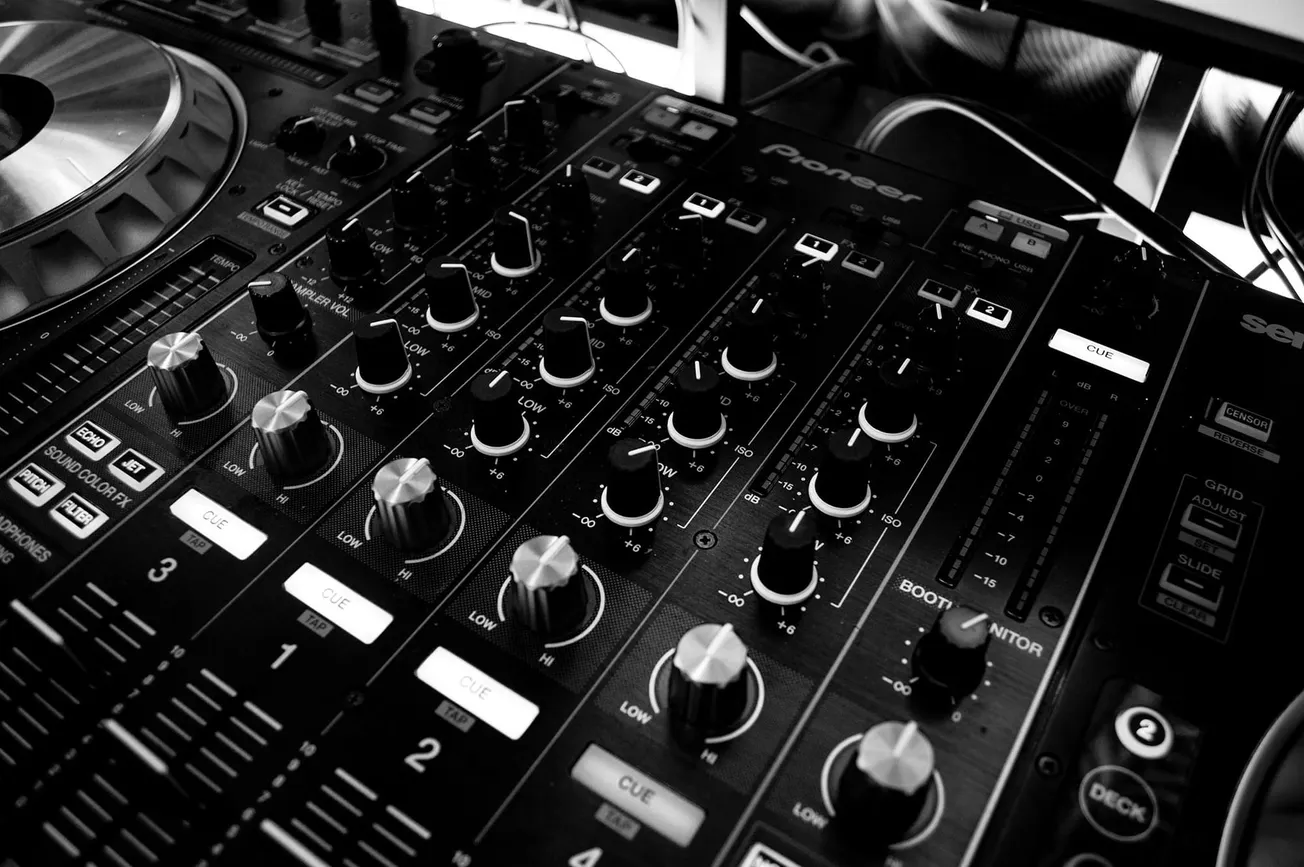 Close-up of a black DJ mixer with multiple knobs, sliders, and controls. The image is in black and white, giving a sleek, modern feel.