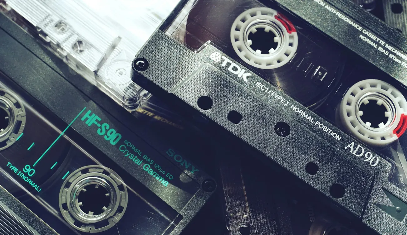 Close-up of stacked vintage audio cassette tapes from brands like TDK and Sony, highlighting the reels and labels. The image evokes nostalgia.