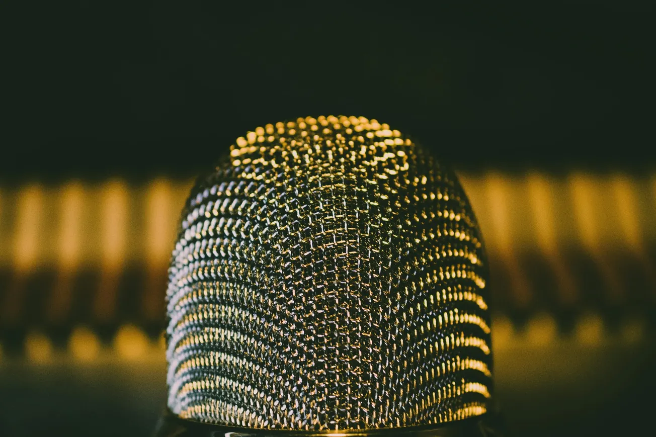 Close-up of a vintage microphone with a textured metal grille, warmly lit against a blurred, gold-toned background, creating a nostalgic ambiance.
