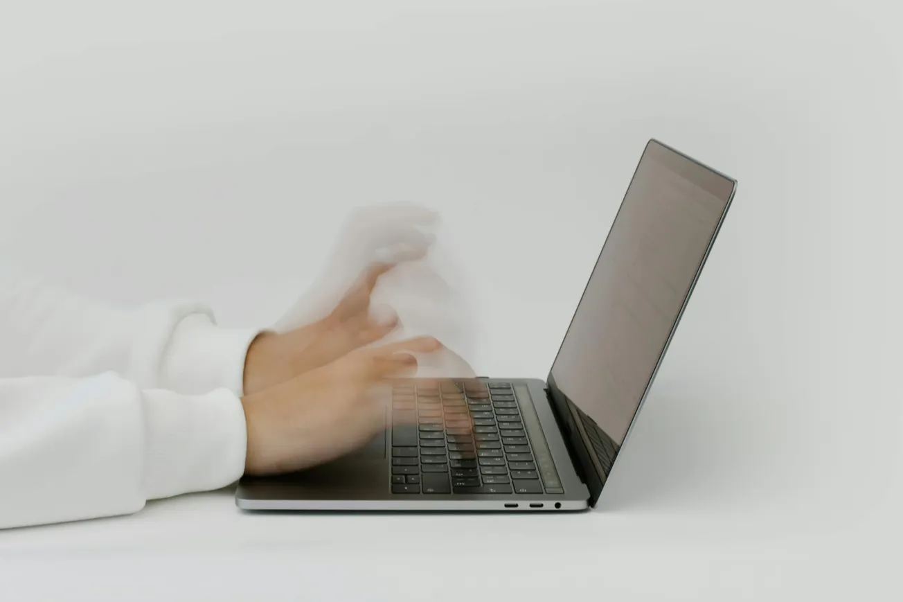 Hands typing rapidly on a laptop with a blurred effect, suggesting speed and efficiency. The background is white, creating a minimalist, focused atmosphere.