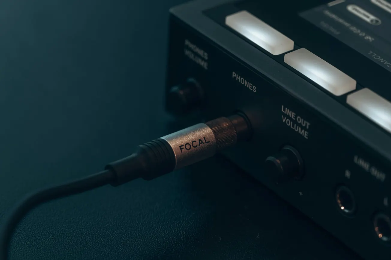 Close-up of a headphone cable labeled "FOCAL" plugged into the "PHONES" jack of a sleek black audio device. Soft lighting creates a focused, professional tone.