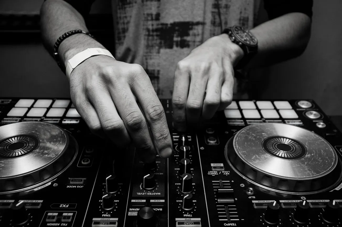 Close-up of hands adjusting controls on a DJ mixer, conveying focus and creativity. The black and white tone adds a classic, artistic feel.