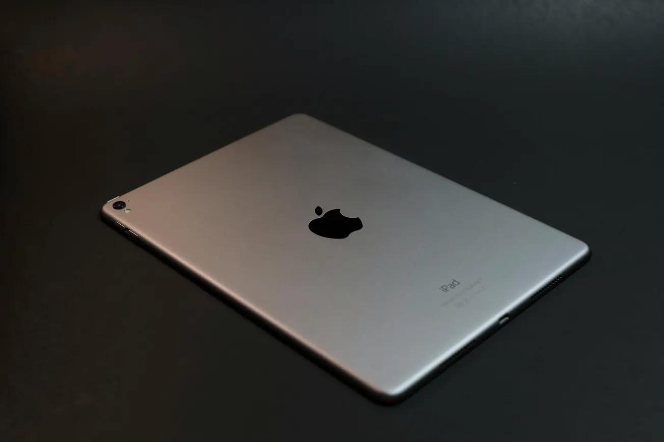The image depicts a sleek, silver iPad resting on a dark surface. It features the Apple logo prominently, suggesting a minimalist and modern aesthetic.