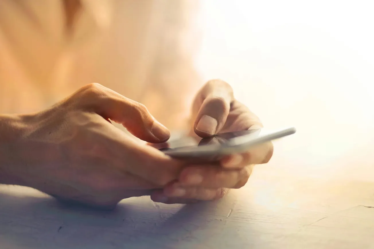 Hands typing on a smartphone against a softly lit background, evoking a calm and focused atmosphere. The image suggests communication and connectivity.
