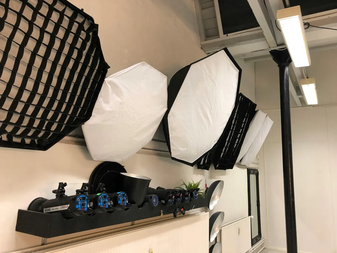 A row of octagonal softbox lights with grids lines a studio wall. Below them are mounted camera rigs and blue valve controls. The tone is professional.