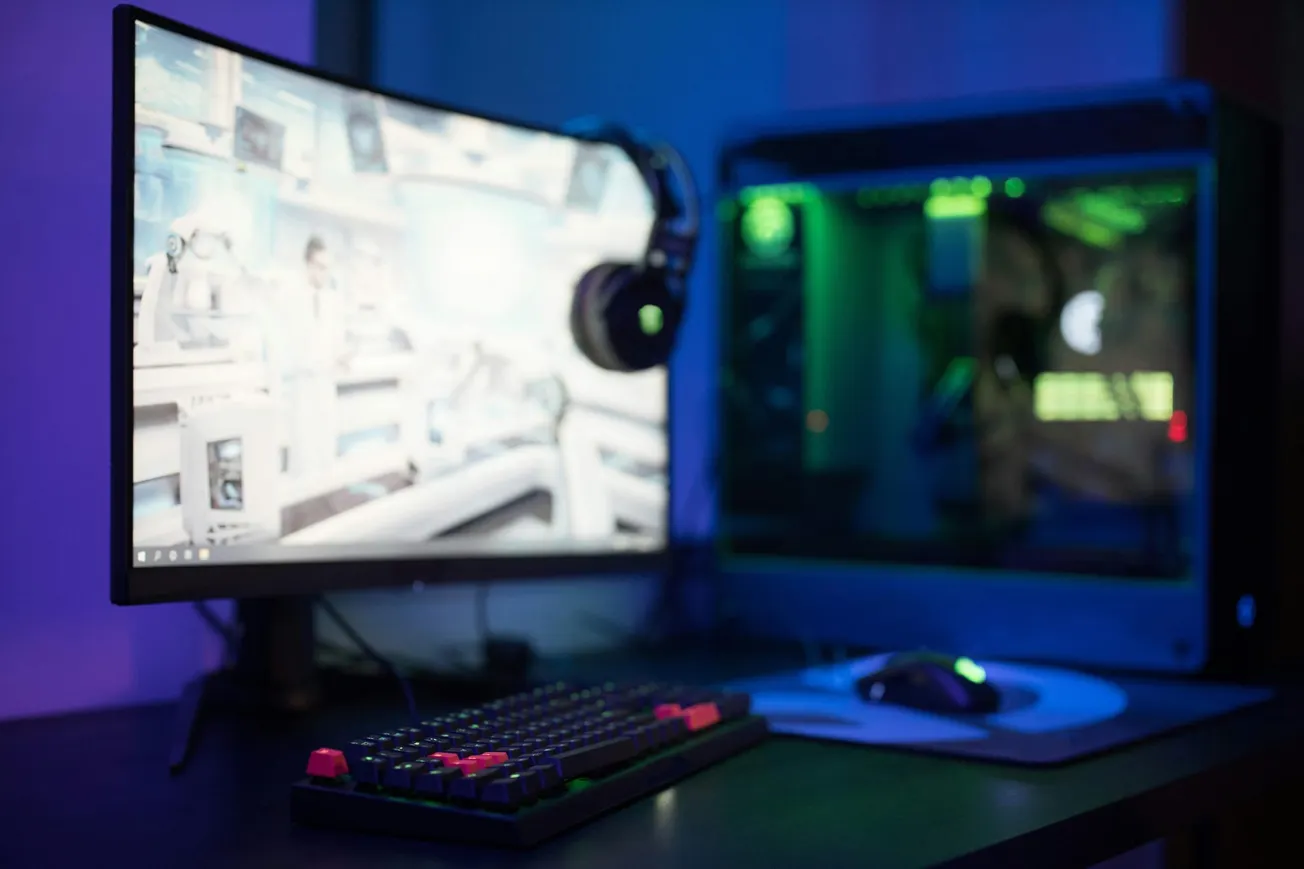 A sleek gaming setup featuring a curved monitor displaying a sci-fi scene, RGB-lit keyboard, mouse, and an illuminated computer tower. 