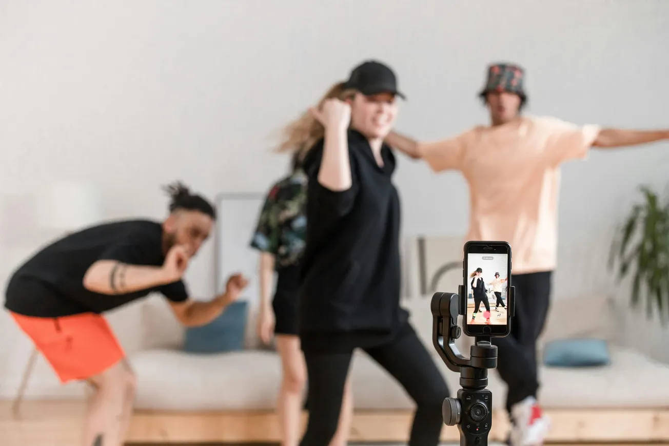 Three people dance energetically in a living room, captured by a smartphone on a tripod. The atmosphere is lively and playful.